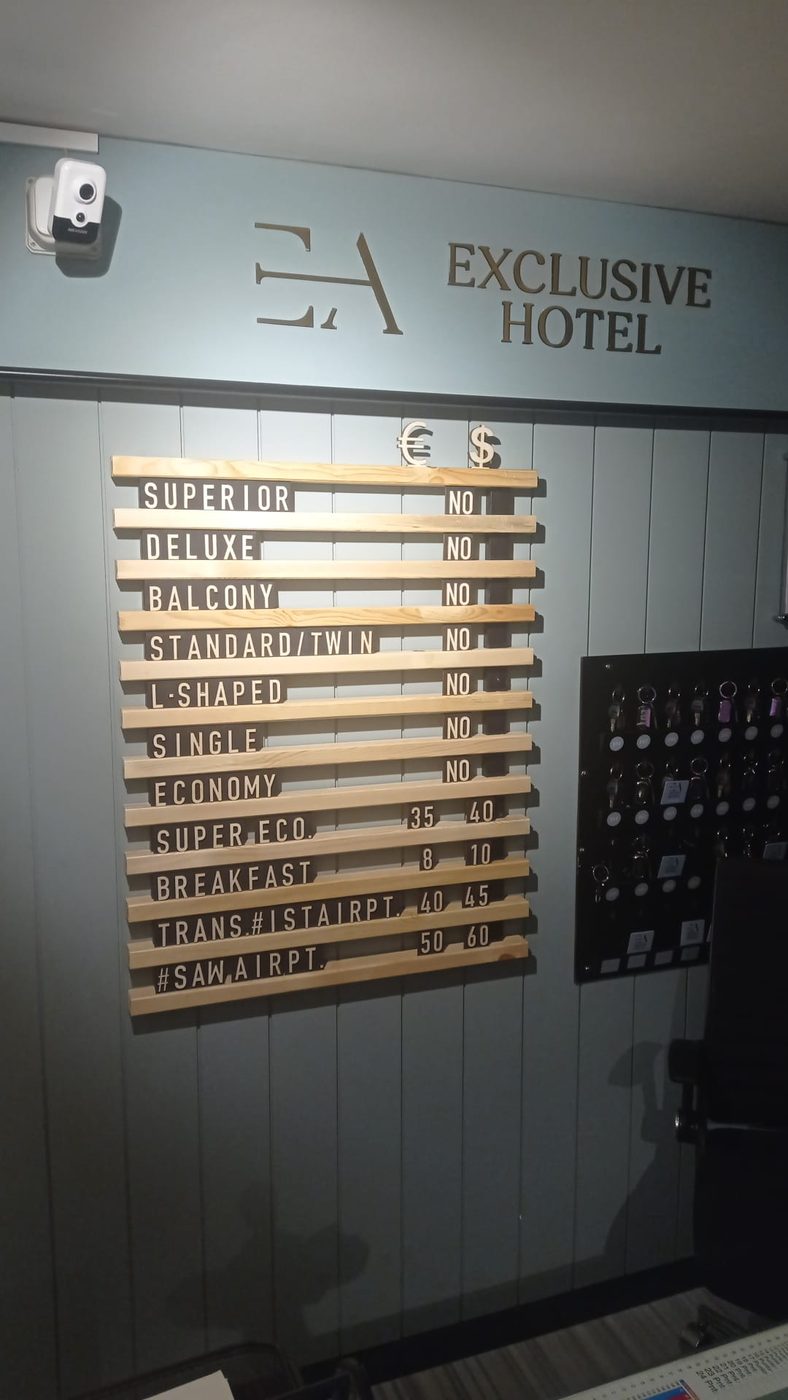 EA Exclusive Hotel İstanbul resepsiyonunda otel fiyat panosu; oda tipleri, kahvaltı ve havalimanı transfer ücretleri